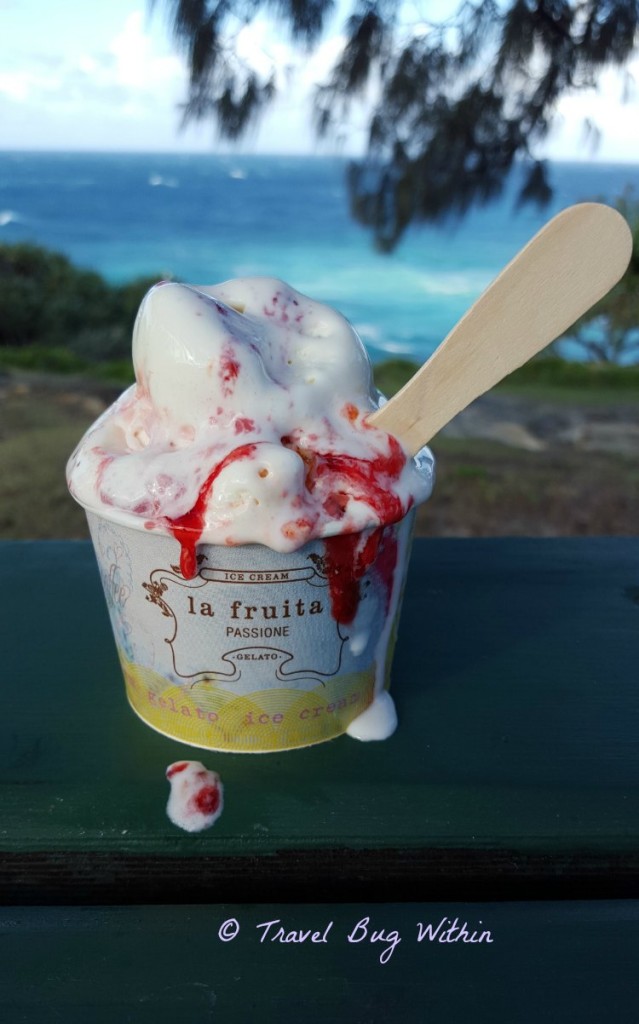 Image of a small tub filled with ice cream and straberry topping with a timber spoon on the side 