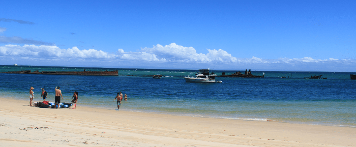 Image of clear blue water and a white beach with boats on the water