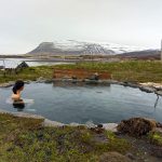 woman sitting in a natural hot spring she is looking towards a snow capped moutain in the distance