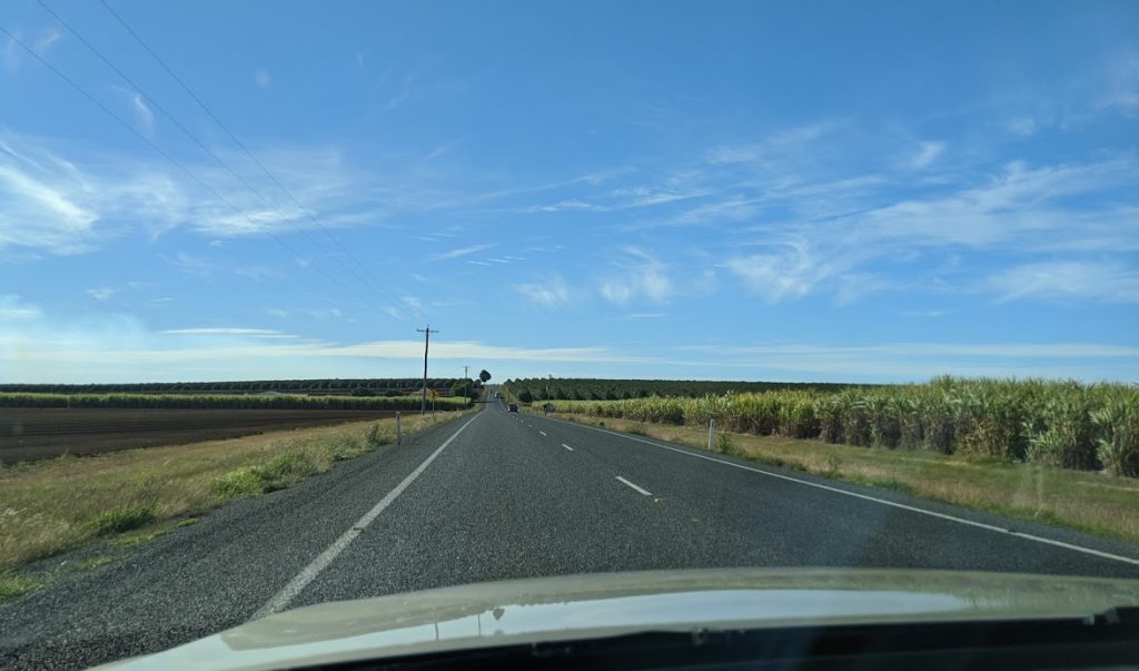 Open bitumen road with sugarcane and farm paddocks on eitehr side 
