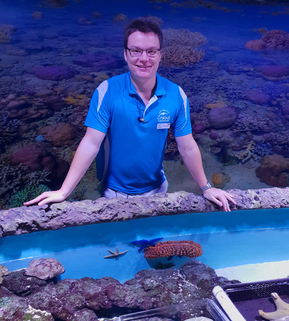Man in blue shirt stands behind tank with starfish and sea urchins