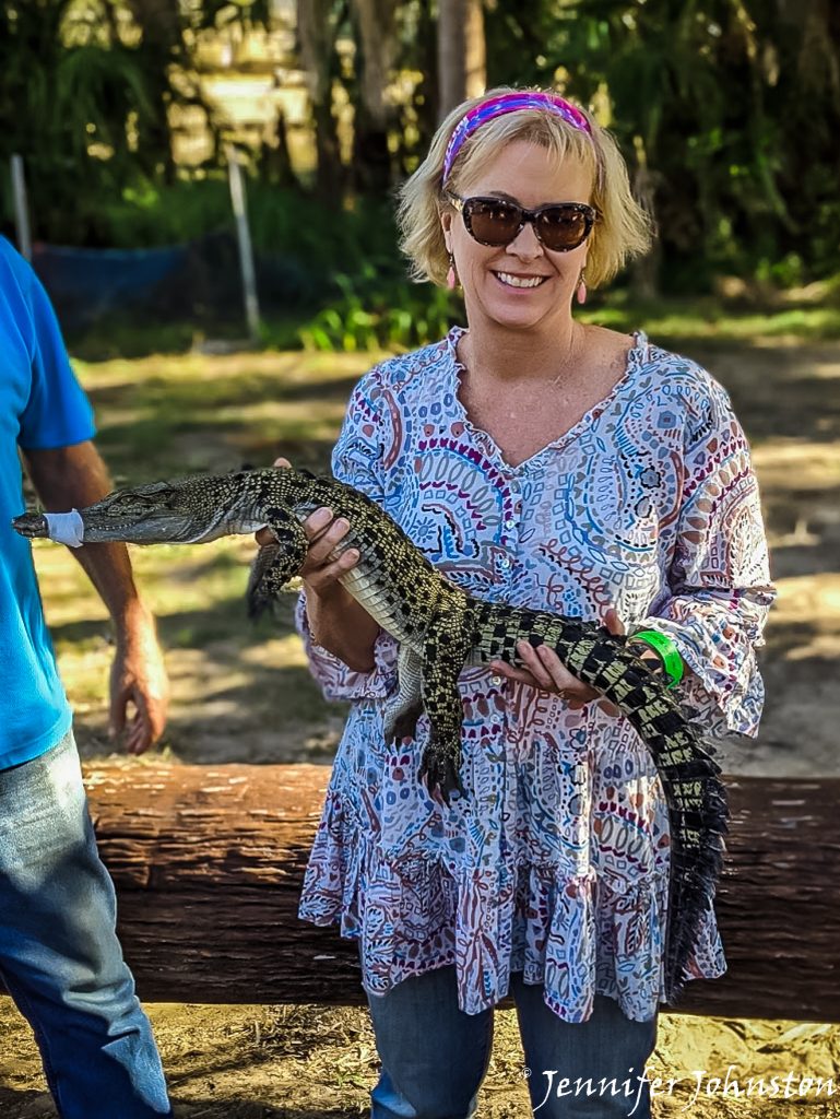 woman in a floral shirt holds a baby crocodile