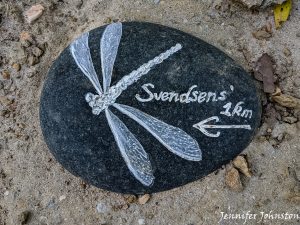 a small grey stone with a dragon fly and the word Svebdesn's and an arrow carved into the surface 
