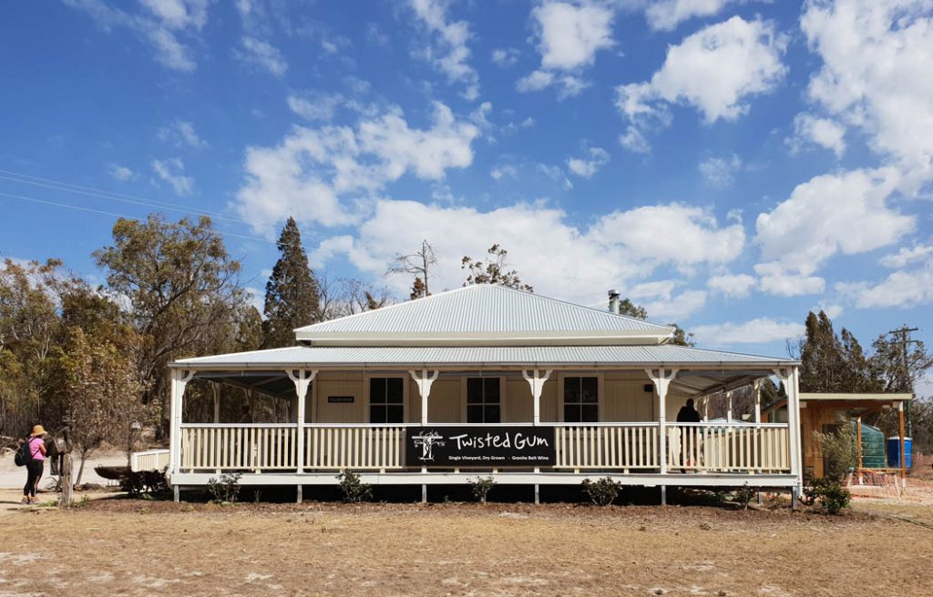 Image of a Queensland style house with wrap around verandas and a corrugated iron roof and sign on the veranda palings that says Twisted Gum