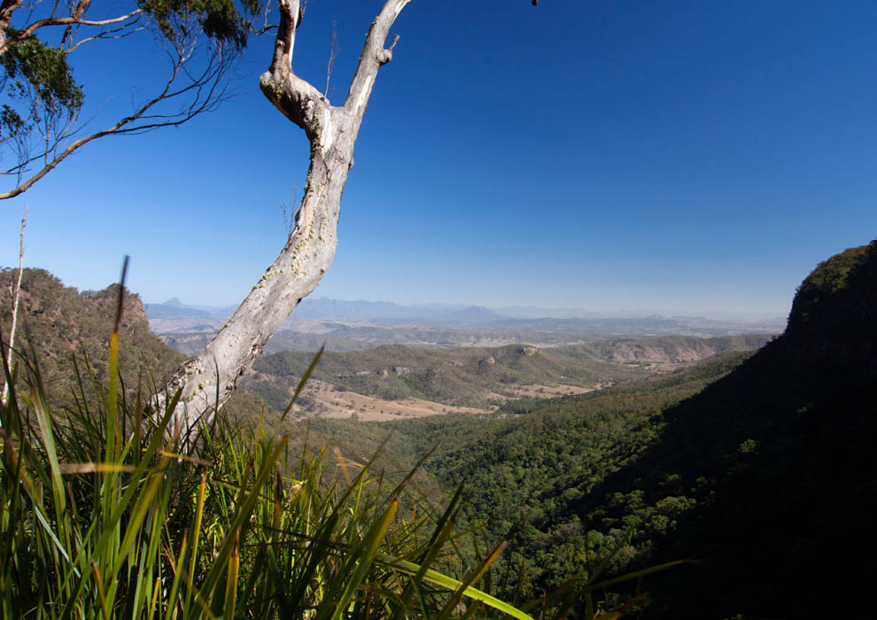 Image showing a sunny day and blue sky photo taken from a lookout with a mountain range in teh background and a plateau in the foreground