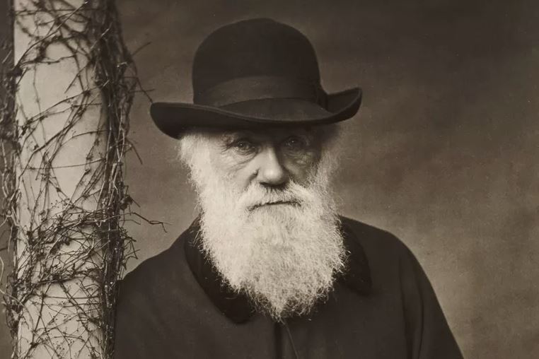 Black and white image of Charles Darwin a man with a white berad wearing a hat