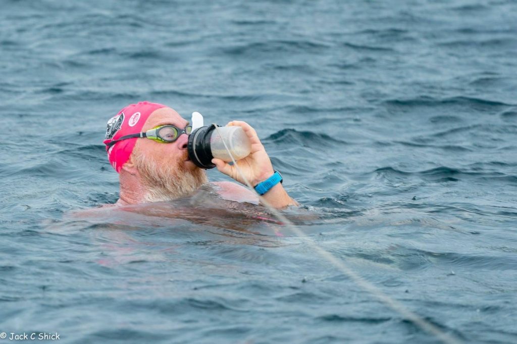 Image of a man treading water in the ocean drinking from a plastic bottle attached to a string
