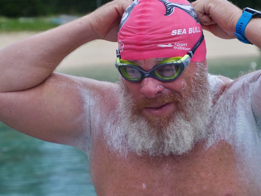 Image of a man with a white beard wearing a pink swim cap that says Sea Bull on the side