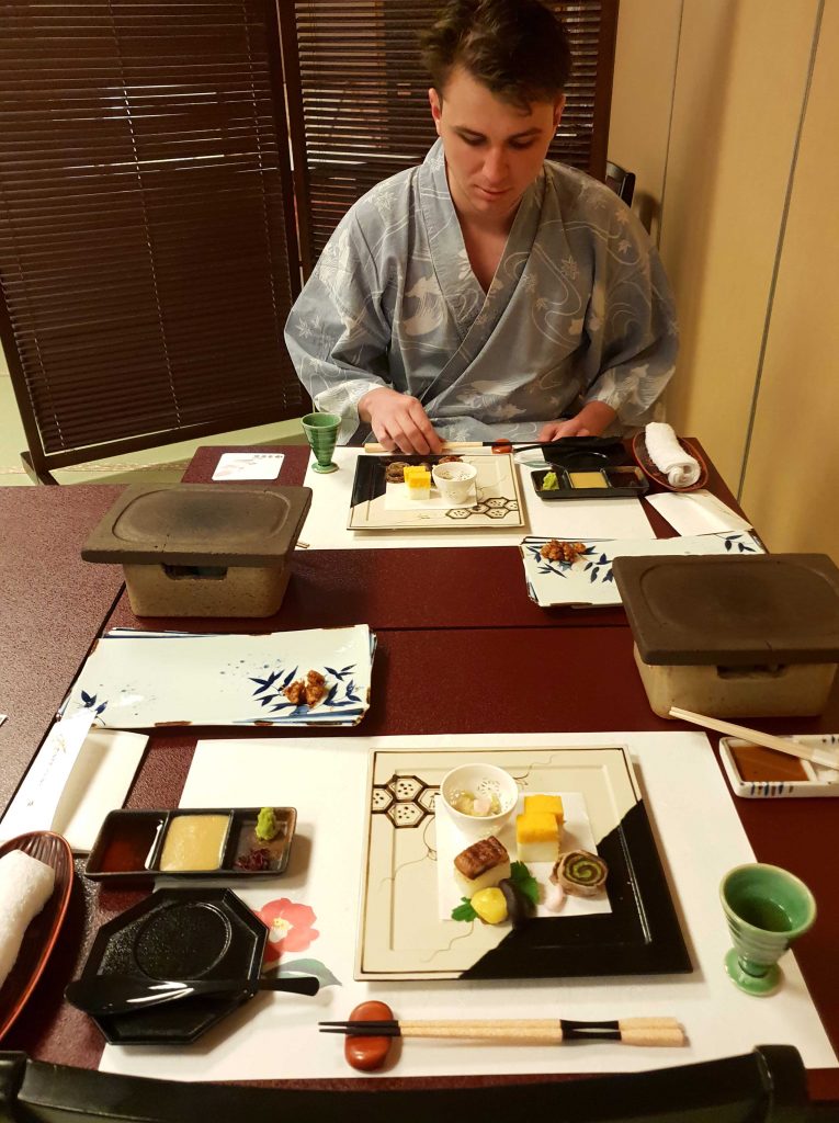 Image of a man wearing a cotton yukata sitting at a table in front of a number of dinner plates