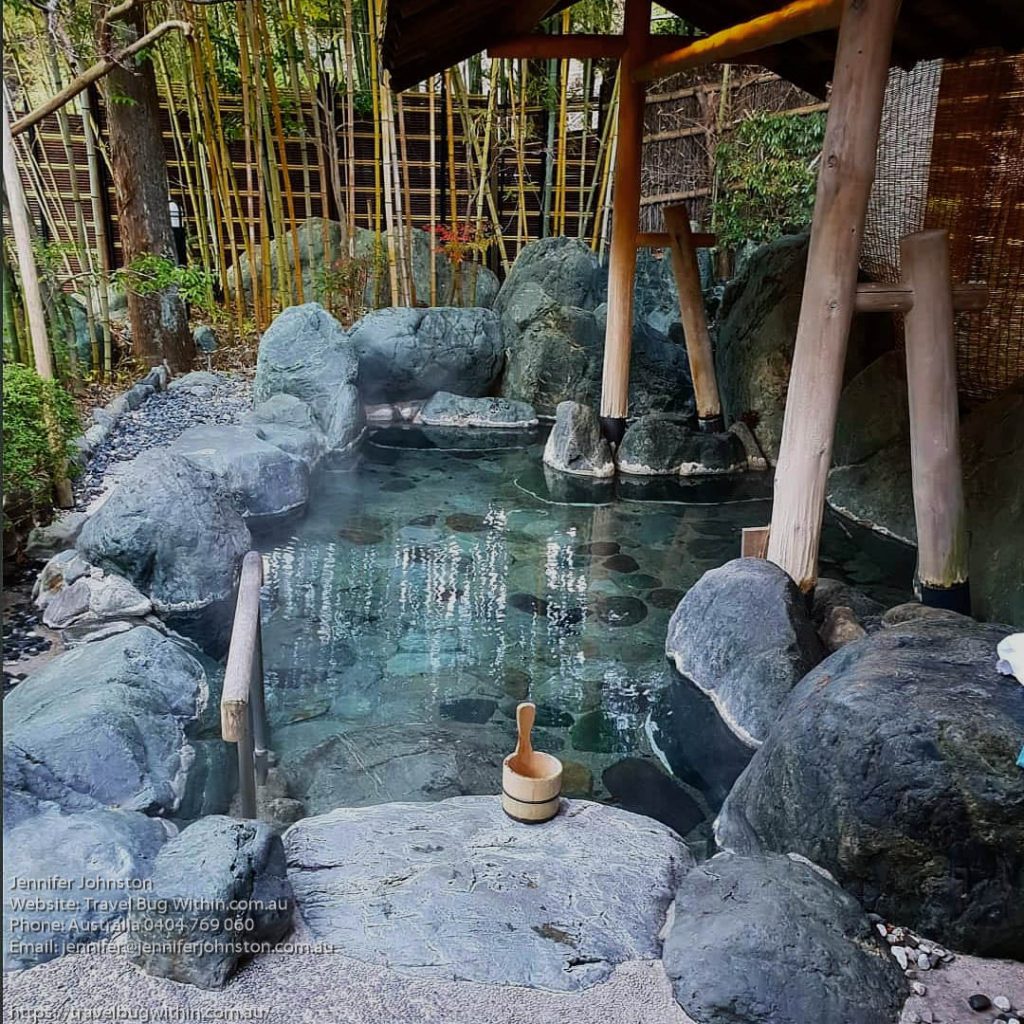 Image of an outdoor onsen bath with stone surrrounds and bamboo poles holding up a roof