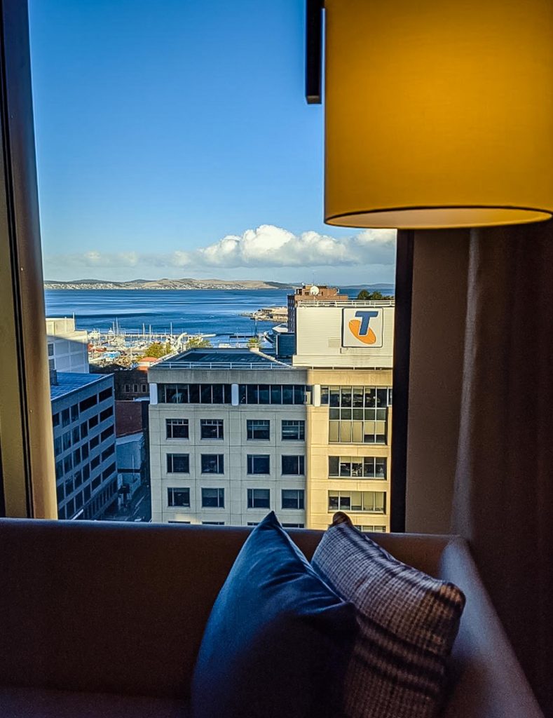 Image of a hotel room window showing a view over buildings then water and mountains in the background