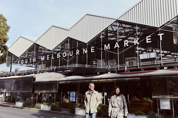 Image of two popel standing in front of a large building with the sign South Melbourne Market on the front