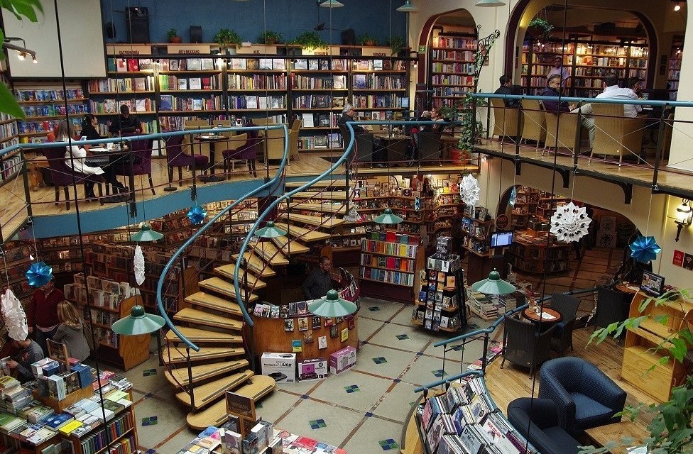 Image of a cafe packed with books on bookshelves and a curved staircase leading up to the first floor