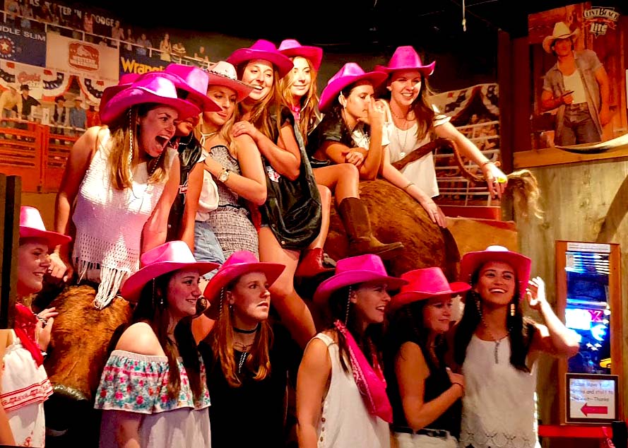 Image of a large group of girls wearing pink cowboy hats smiling as their photo is being taken