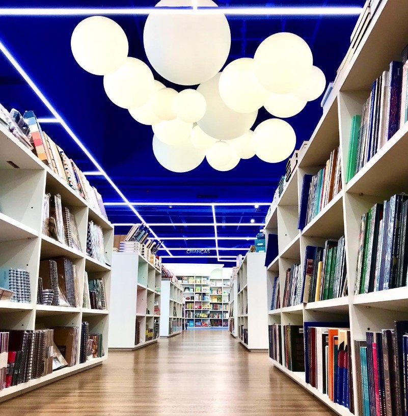 Image of the interior of a bookstore with a bright blue cieling large while balloon lights and white bookshelves filled with books