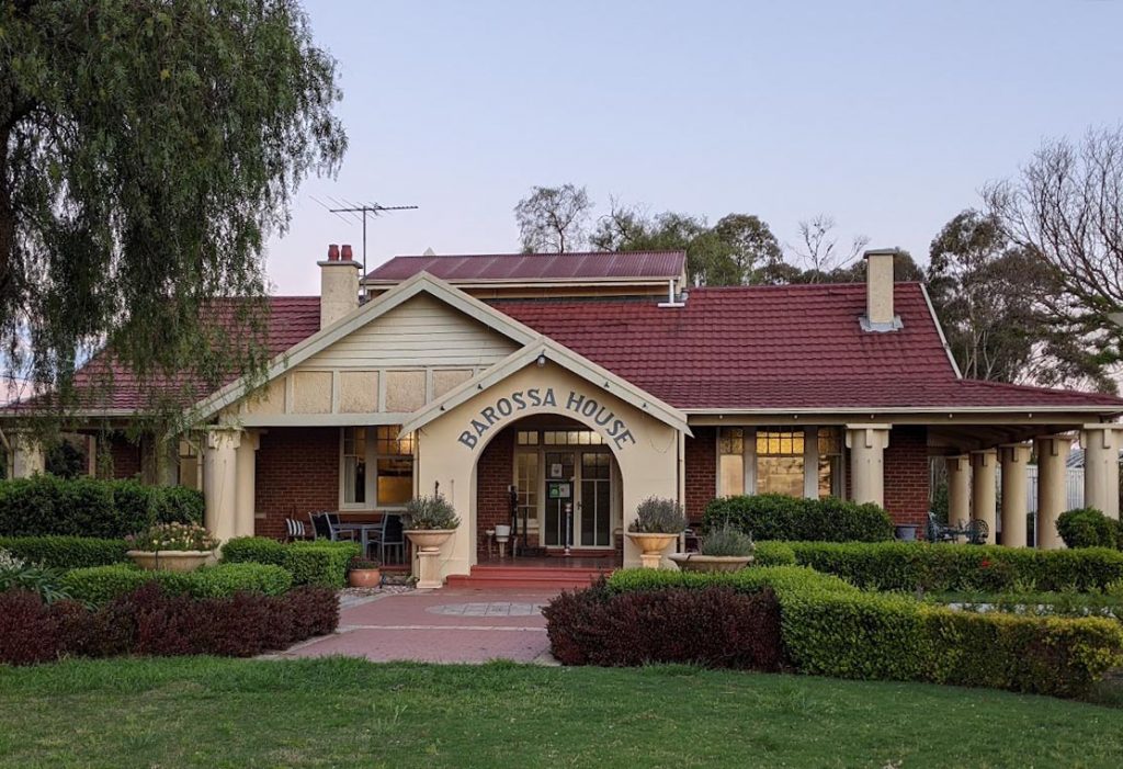 Image of a low set house with red tiled roof and words Barossa House on the front of the house
