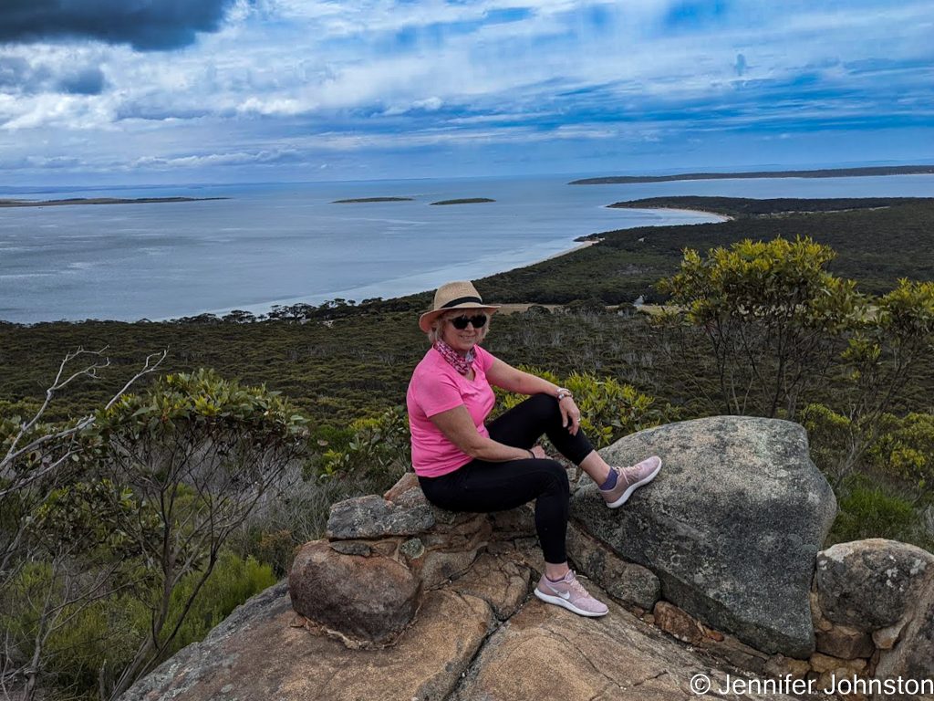 Image of a woman sitting on a rock on a hill with the view of the ocean behind her