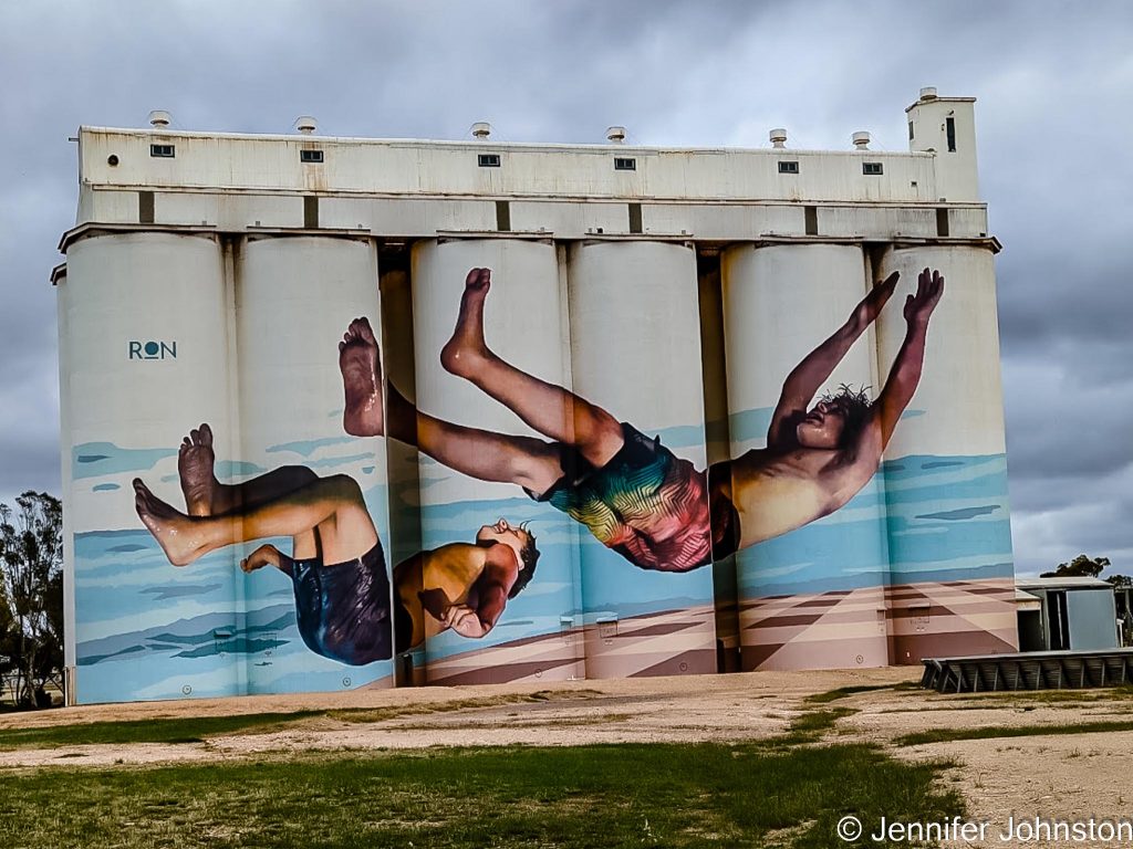 Image of a silo painted with a mural of two young boys jumping into the water