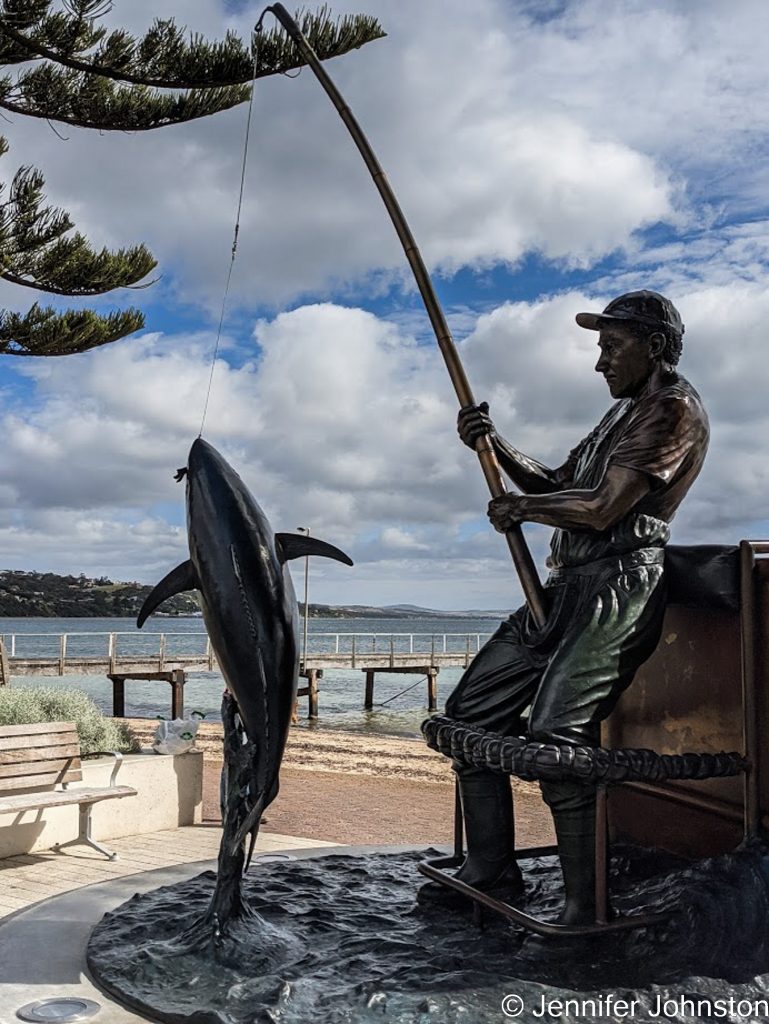 Image of a bronze sculpture of a fisherman with a fishing pole and a tuna fish on the end of the line