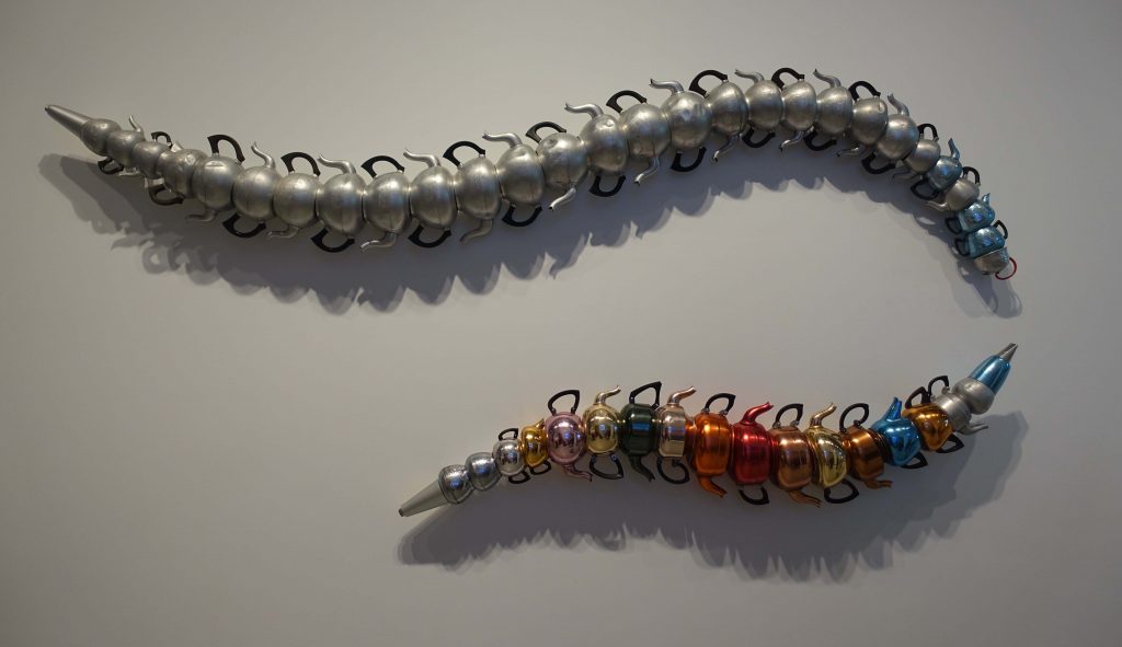 Image of art hanging on the wall - a number of old teapots joined together to look like a large worm