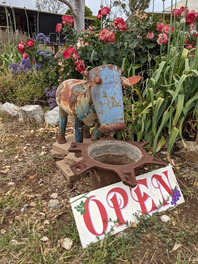 Image of a metal sculpture of cow in a garden standing in front of a sign that says open