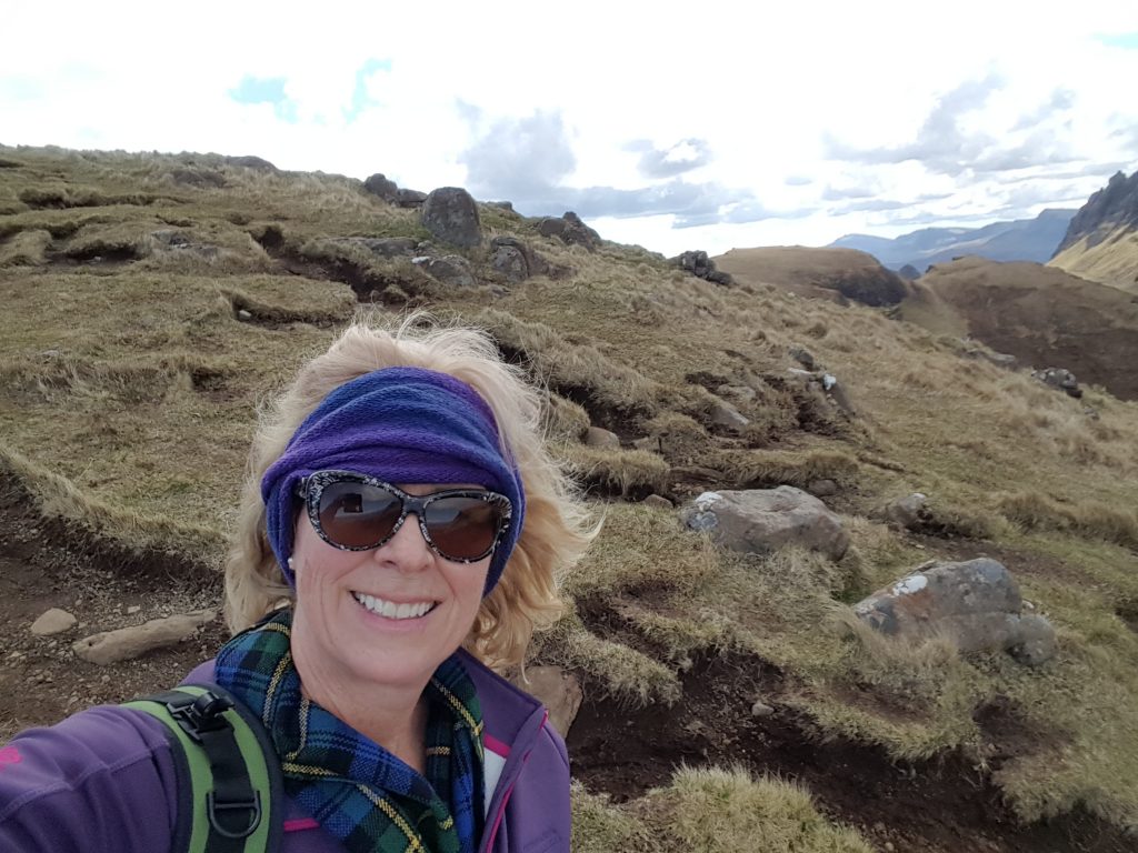 Image of a woman hiking on a mountain, She is wearing a jacket and a tartan scarf