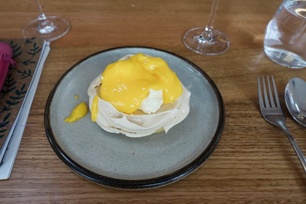 Image of a plated desert a pavlova with a large dollop of yellow lemon curd