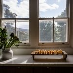 Image of two dozen eggs in a wooden egg holder on a bench top near a window