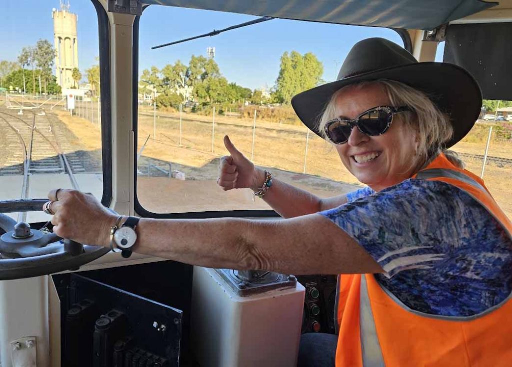 Image of a woman wearing a blue hat and high vis vest sitting in the driver's seat of a train