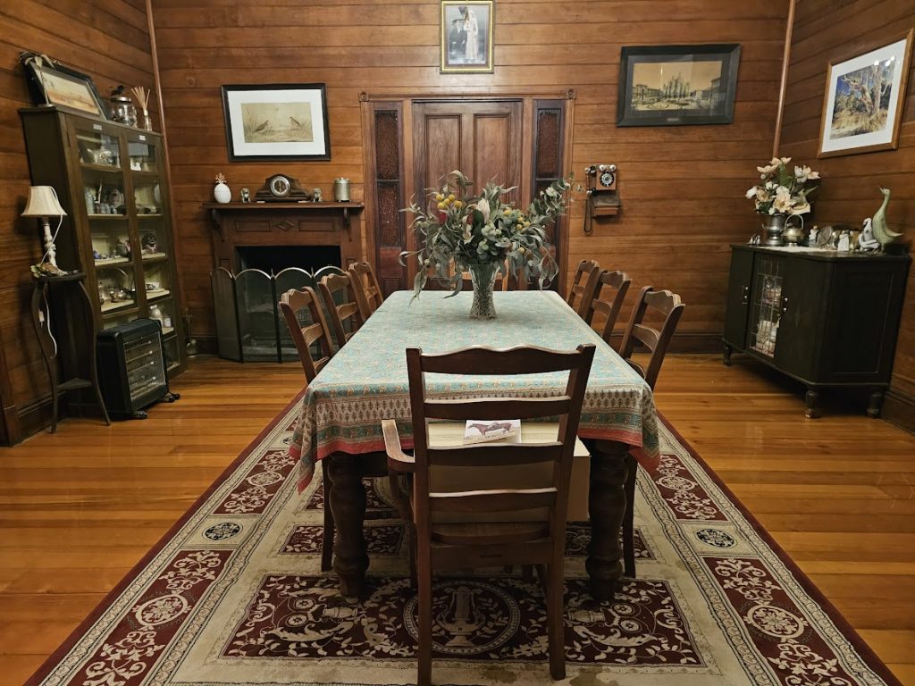 Image of a historic older style room with timber floor and a long timber table with tablecloth and a vase of flowers on the table