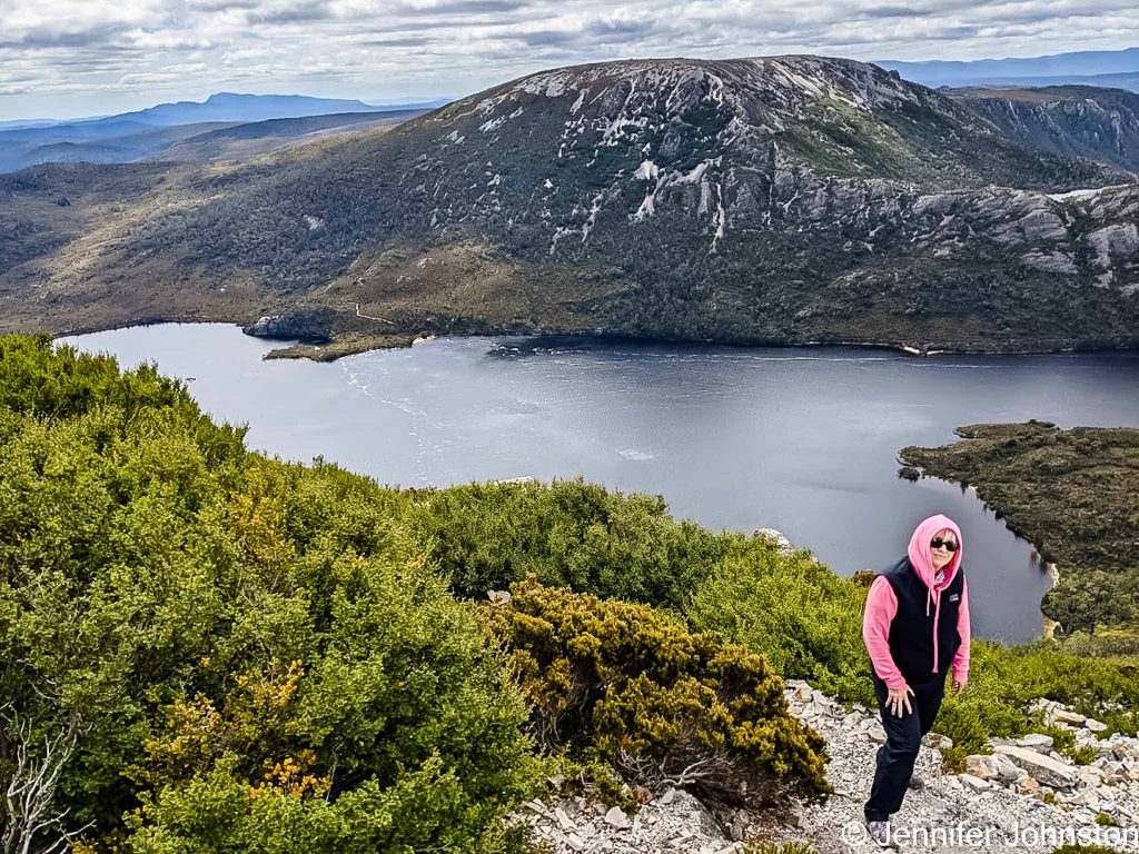 Image of a woman standing on a cliff top with a lake and smaller mountain in the background