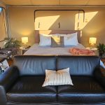 Image of the inside of a glamping tent showing a queenssize bed and a black leather sofa
